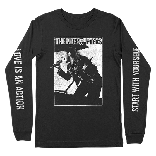 The Interrupters Official Merchandise. 100% black cotton t-shirt with a black and white photo of Aimee Interrupter singing on the front and the lyrics "love is an action, start with yourself" from the song "As We Live" printed down the sleeves.